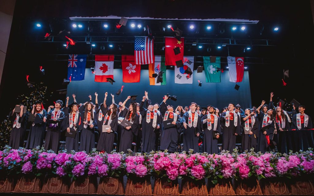 Graduates of the American International School of Guangzhou (AISG) celebrate at commencement beneath the flags of their school community, at the first international school founded in southern China